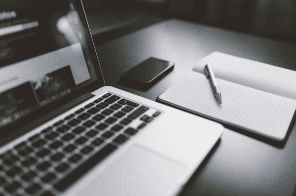 Laptop on a desk with notebook and pen.