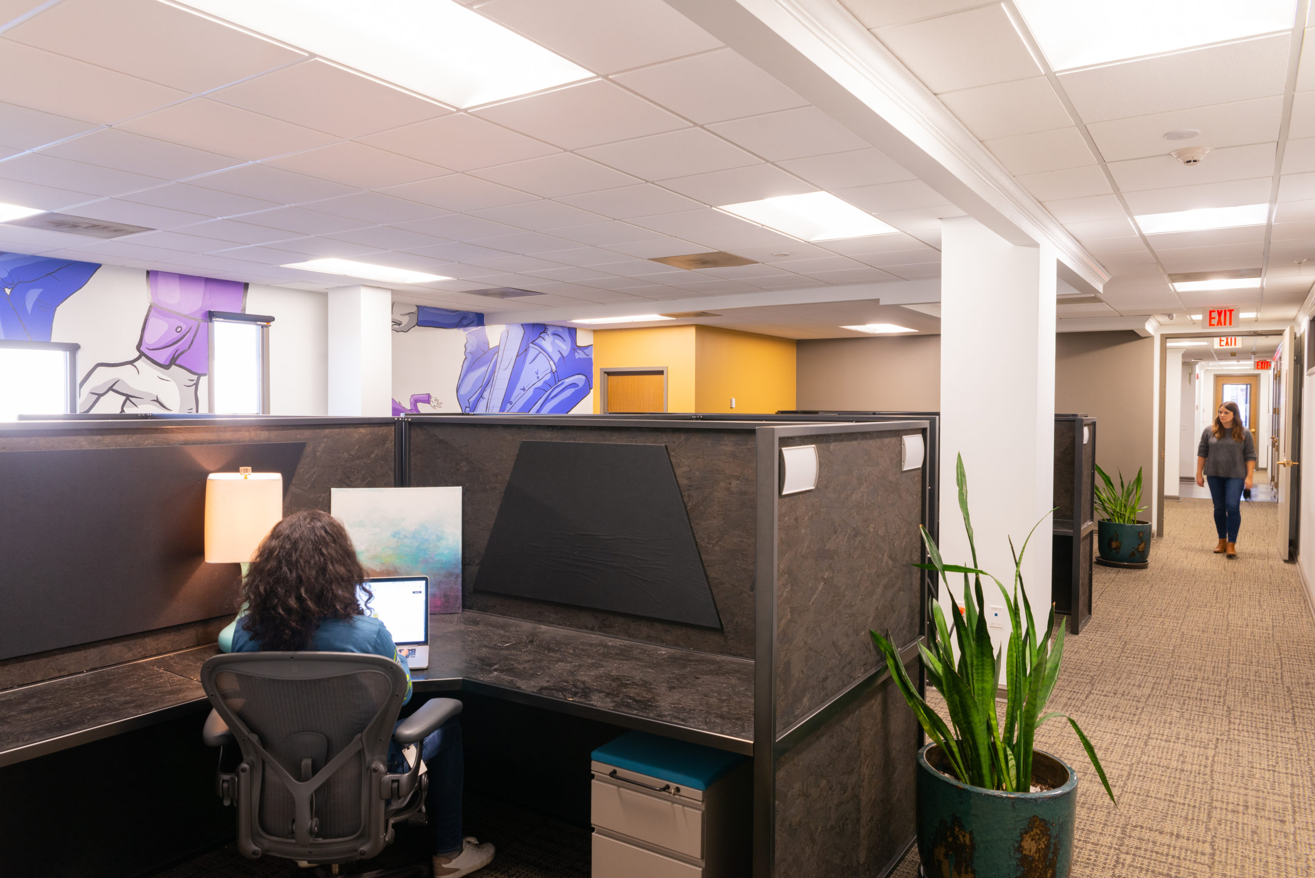 Woman working at a brown cubicle in a large office.