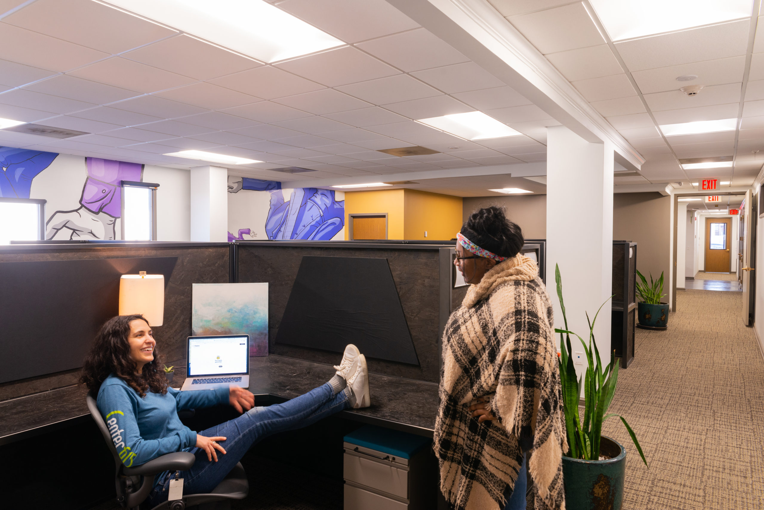 Two women talking in a cubicle.