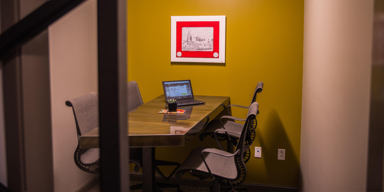 Meeting room with five chairs around a desk and an open laptop.